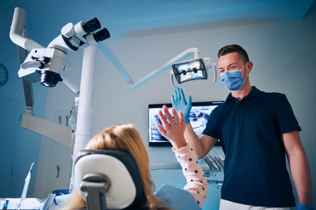 Dentist giving high-five to girl in modern dental surgery